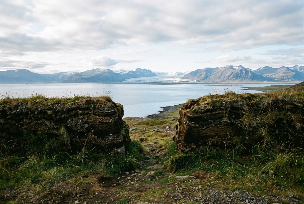 A gap in a turf wall opening onto a broad Icelandic bay with a distant glacier, long low light
