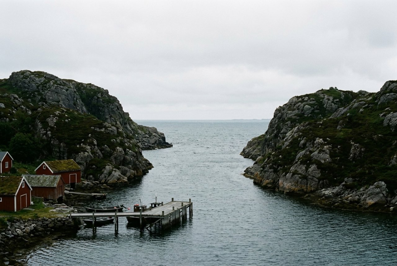 A narrow sound between two steep granite islands opening onto open Norwegian sea, a wooden jetty, flat northern light